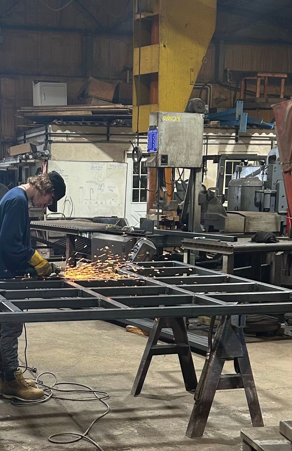 Welder in blue shirt and gloves using a torch on metal, creating sparks in a workshop.