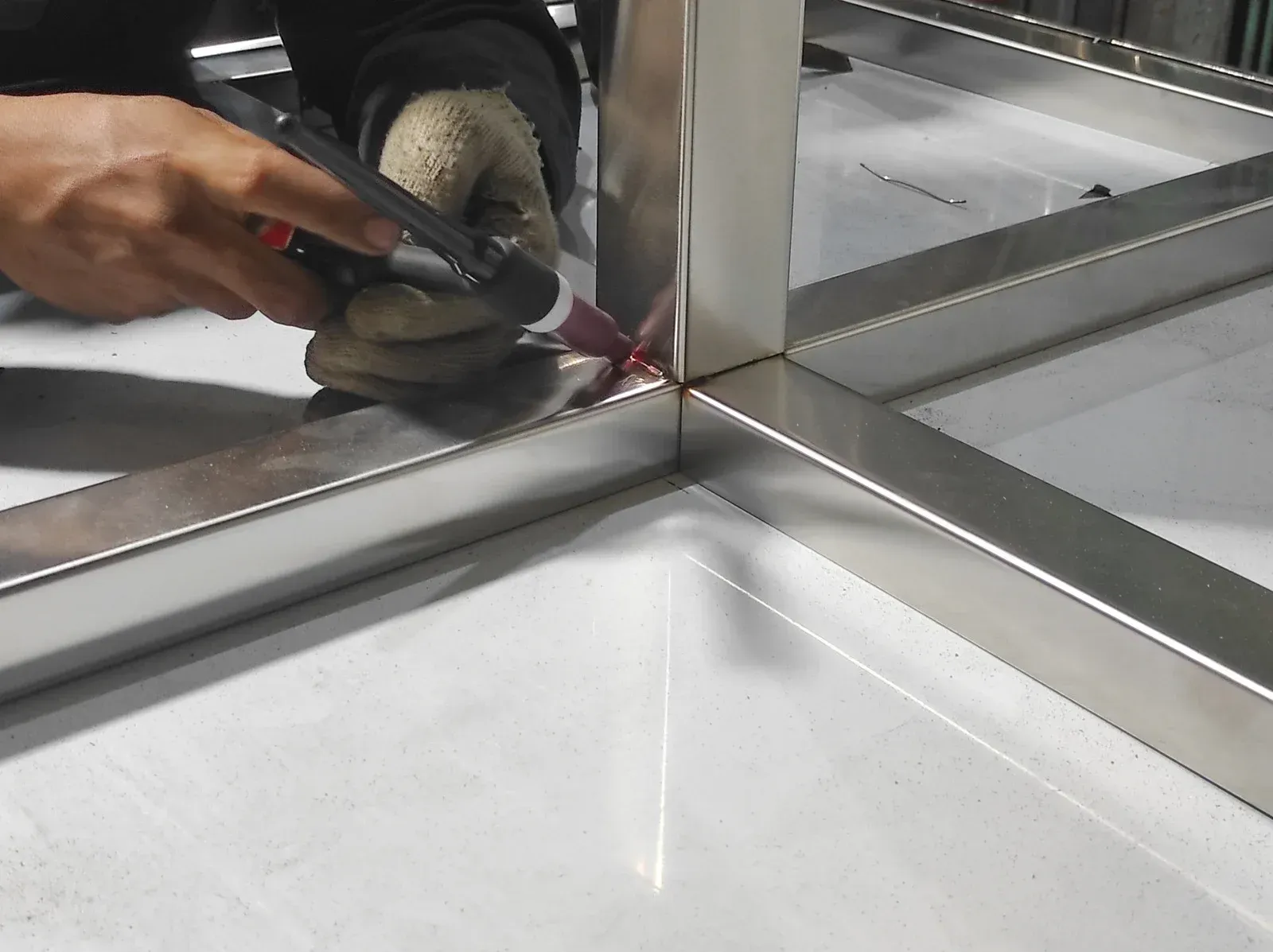 Person welding metal frame with a torch, wearing gloves.