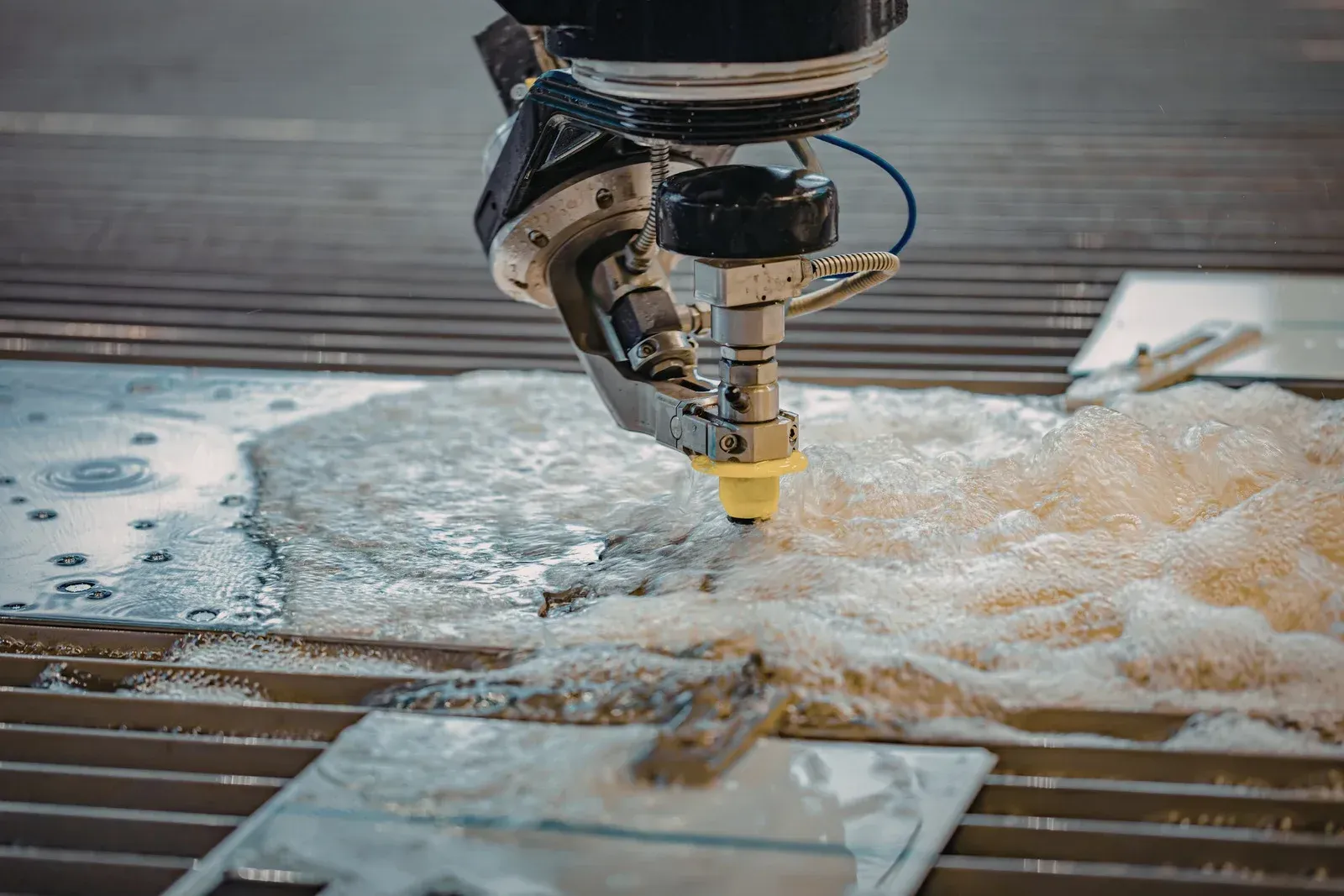 Water jet cutting metal sheets in a factory setting, producing foam around the cutting head.