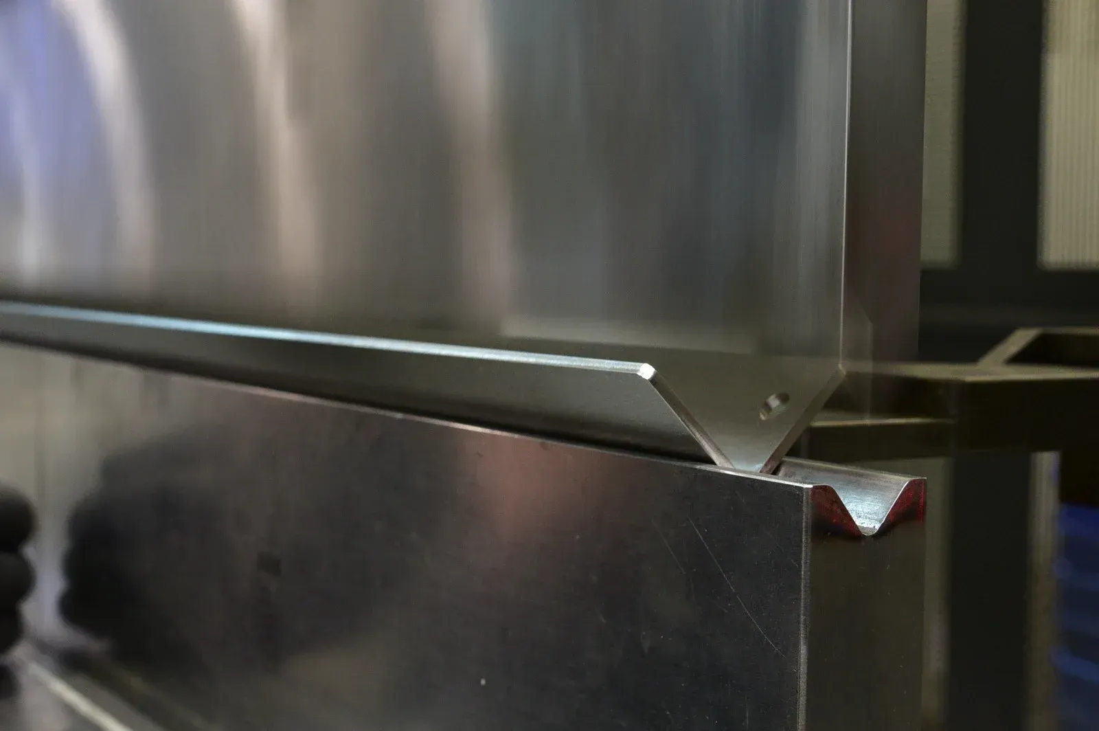 Metal sheet being bent by a machine, forming a right angle.