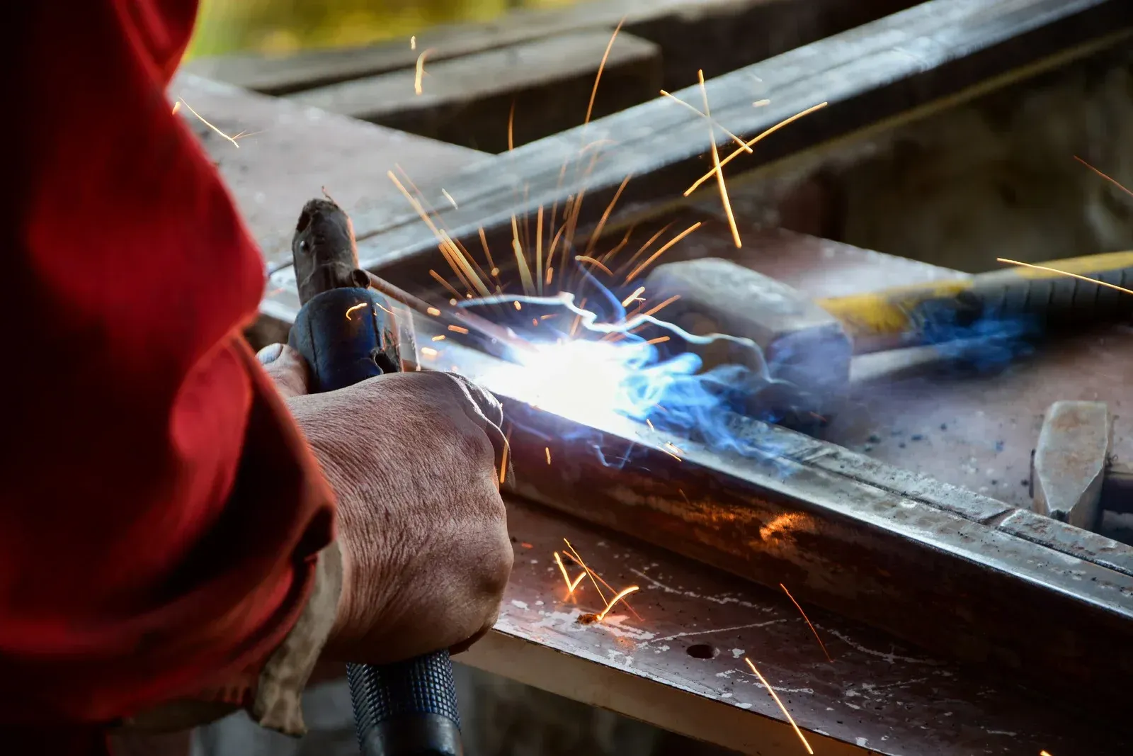 Person welding metal with bright sparks in a workshop setting.