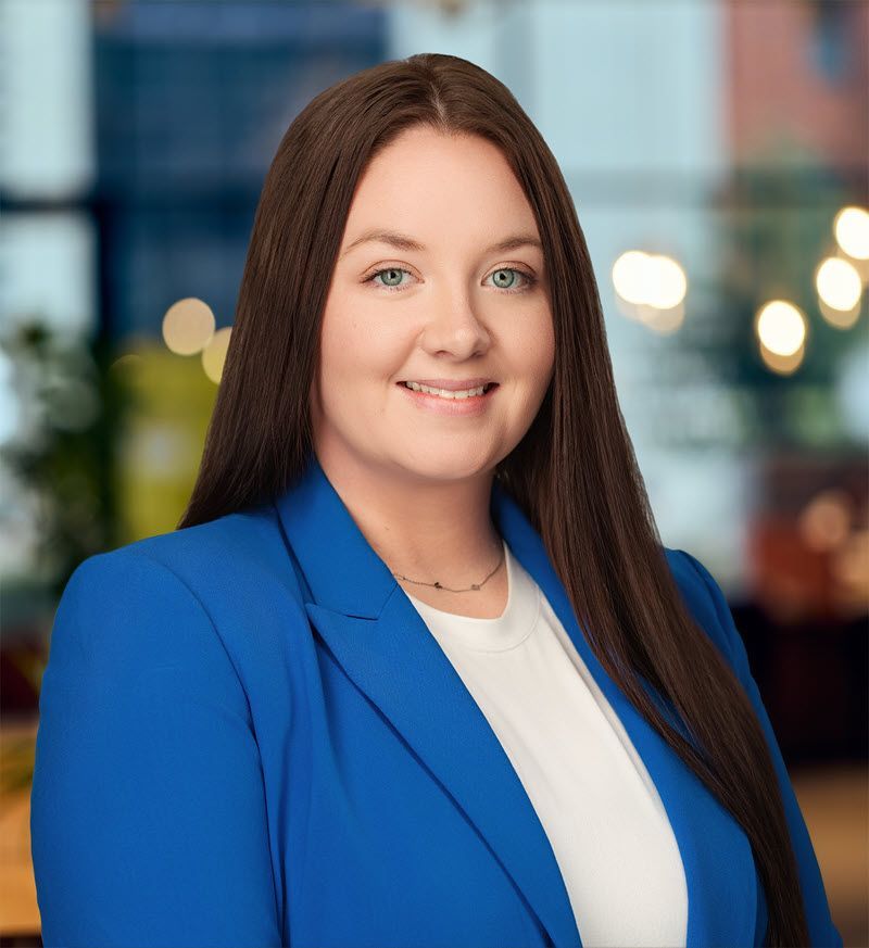 Woman in blue blazer, smiling, with long brown hair, in an office setting.