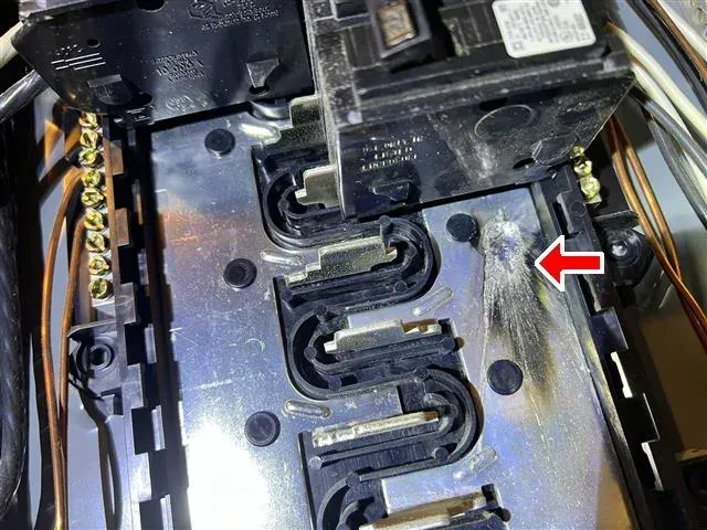Electrical panel with a circuit breaker showing burn marks near the connections, indicated by a red arrow.