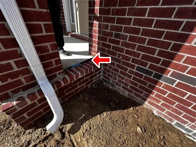 Red brick building with a white gutter and soil, red arrow pointing to a blue-grey foundation step.
