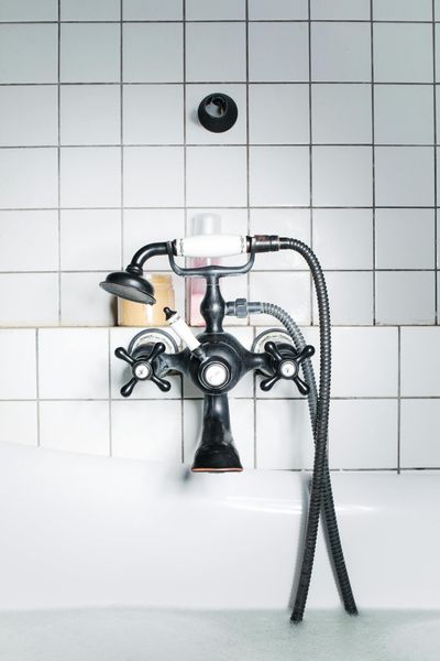 A vintage black faucet over a white bathtub, soap and shampoo on a shelf, white tiled wall.