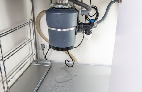 Under-sink view of a garbage disposal with water droplets on the cabinet floor.