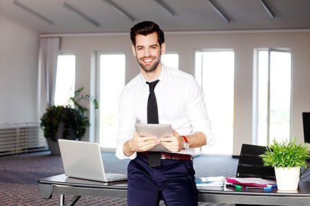 A man is sitting at a desk in an office holding a tablet.