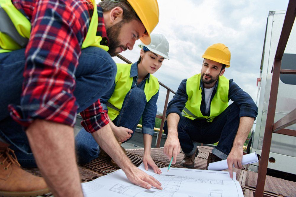 Three Workers  In Hardhats Working With Blueprints — Wendy's Safety Services In Alice Springs, NT