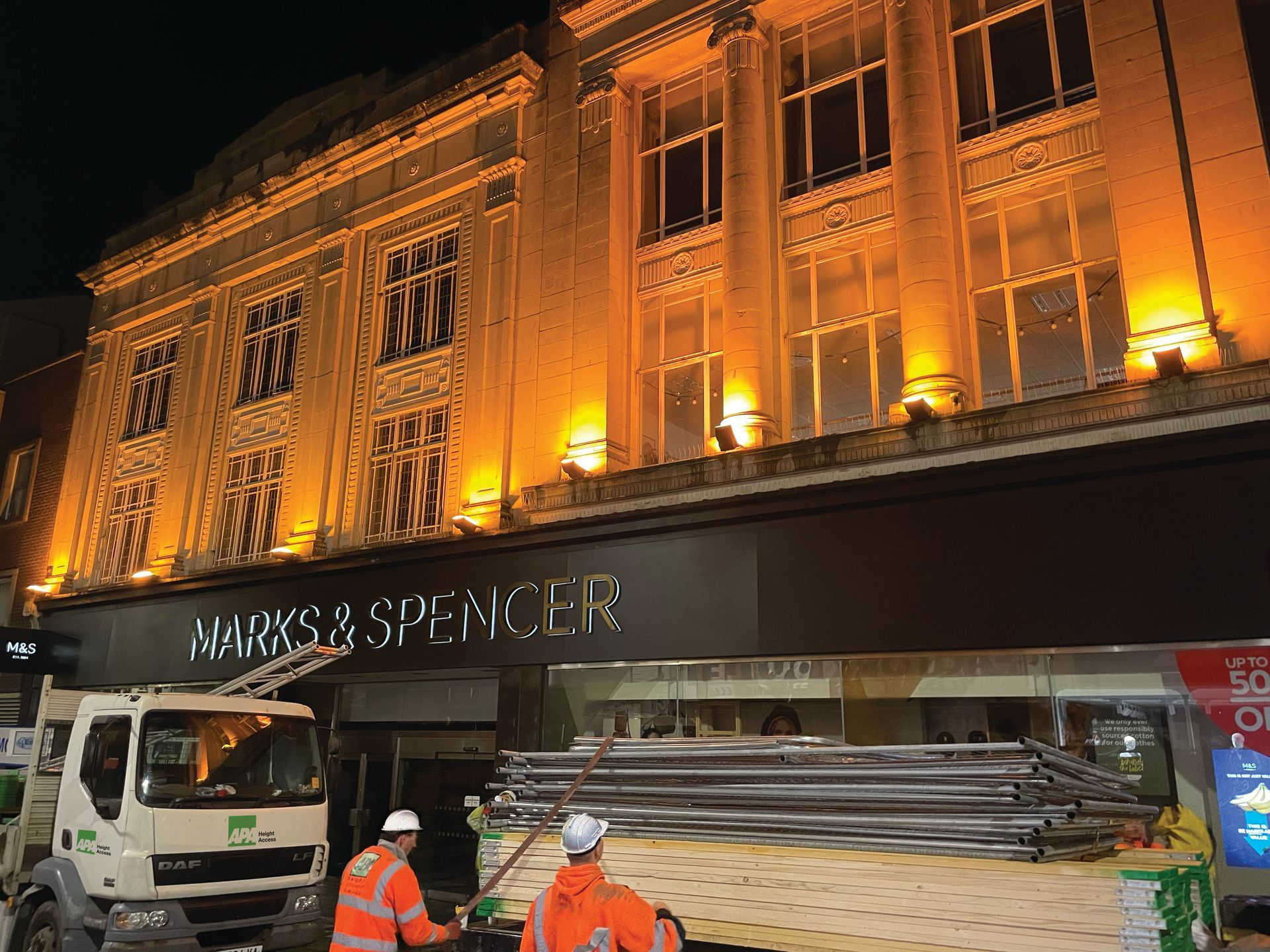 A large building with a sign that says marks & spencer is lit up at night.