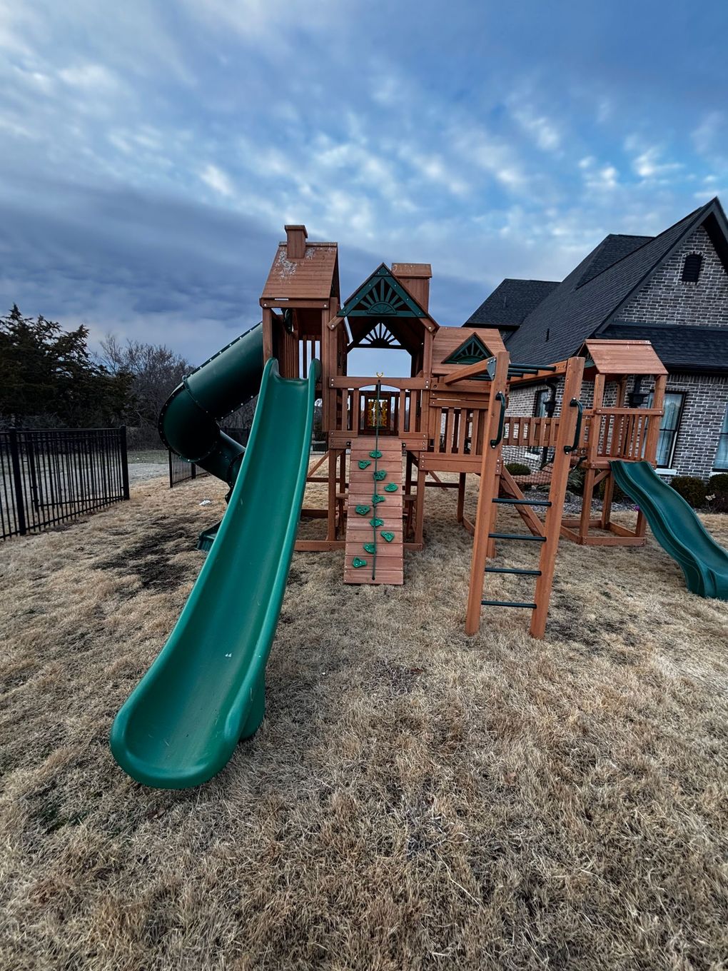 A wooden playground with a green slide and stairs in front of a house.