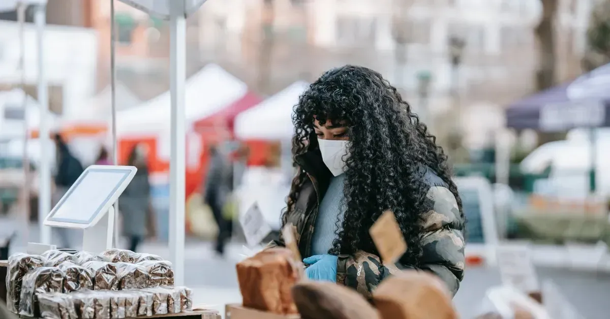 A woman wearing a mask is standing in front of a bakery.
