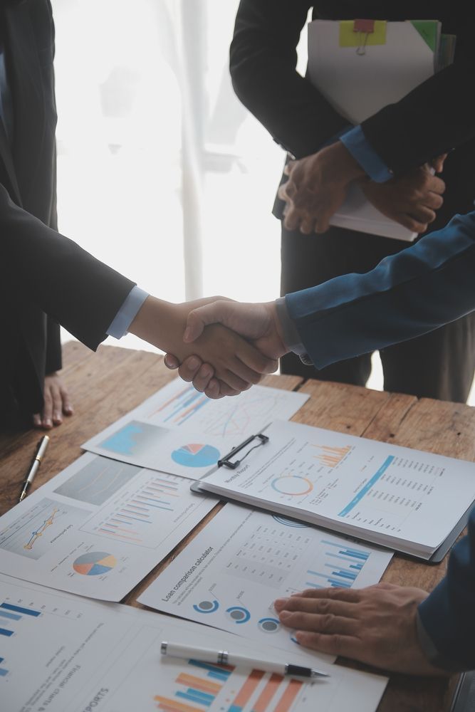 People shaking hands over a table with financial documents.