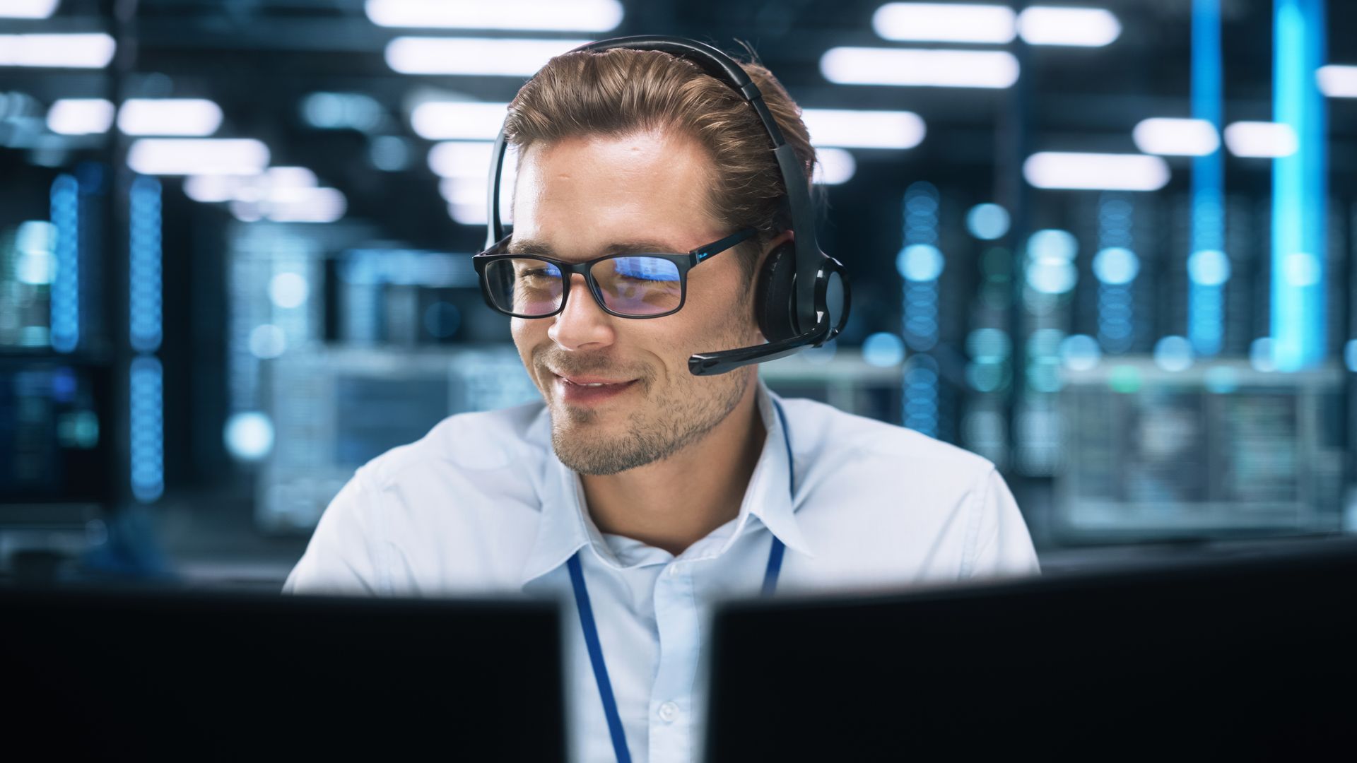 A man wearing headphones and glasses is sitting in front of a computer.