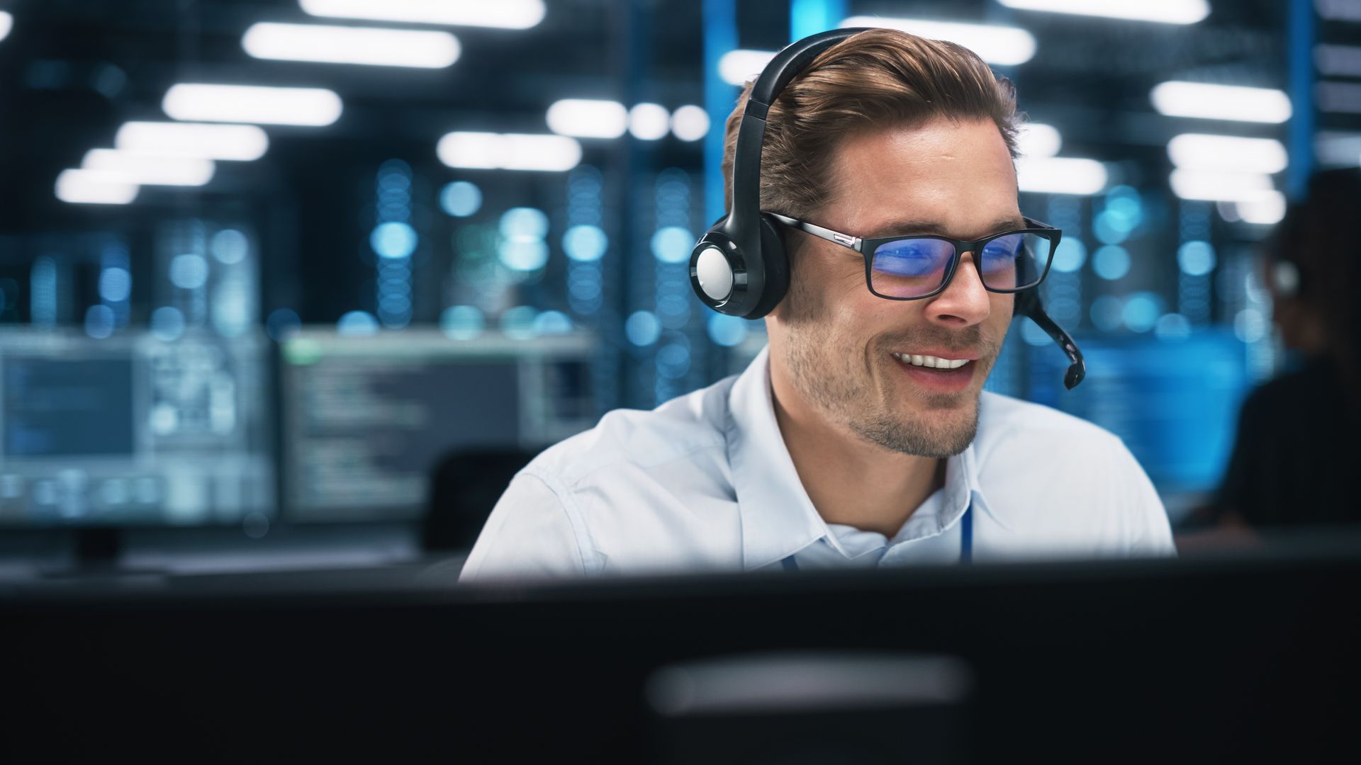 A man wearing headphones and glasses is sitting in front of a computer.