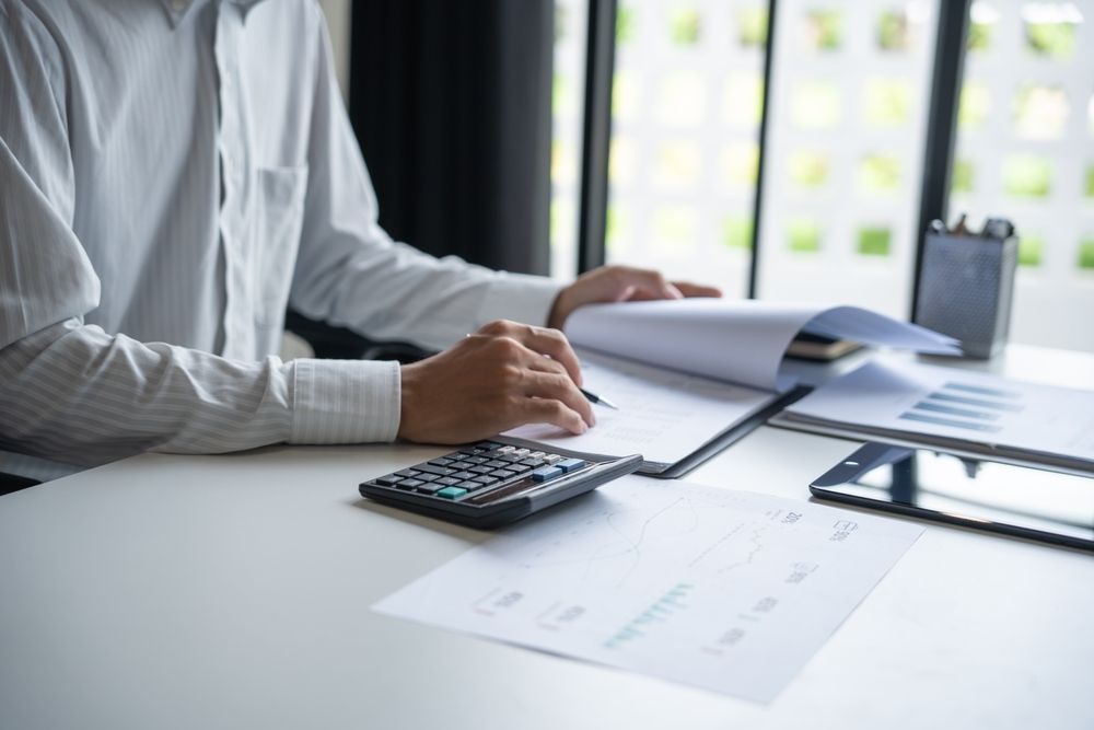 A person in a white button-down shirt working at a desk with a calculator, documents, and a tablet.