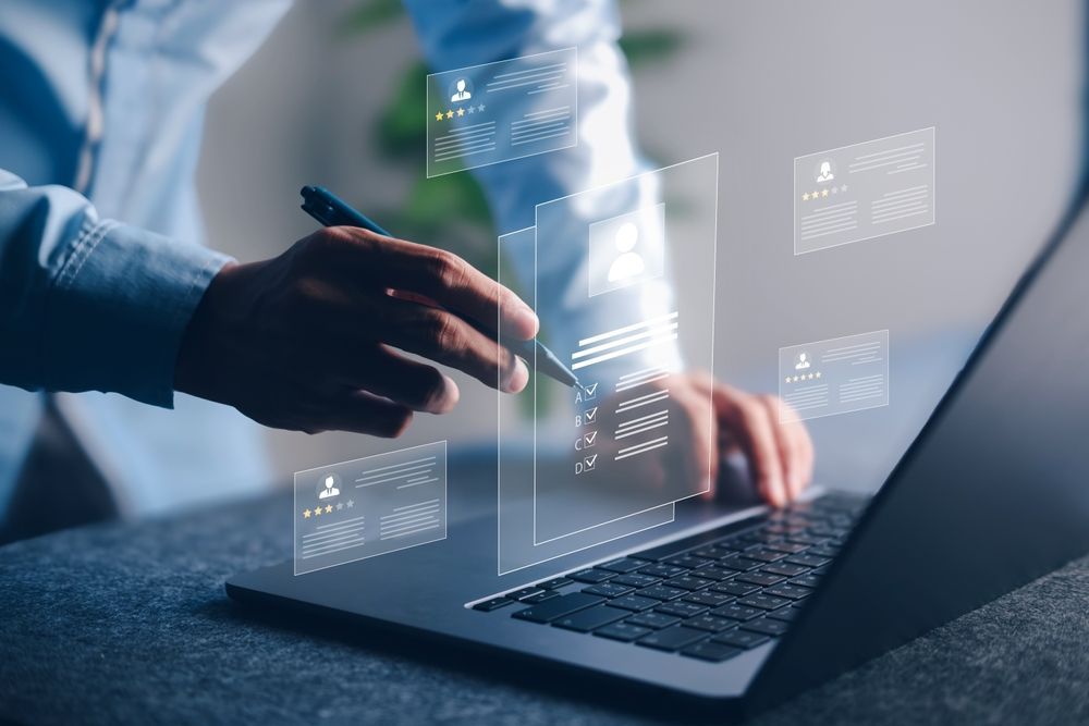 Hands using a stylus on a laptop with translucent data charts overlayed on the screen.