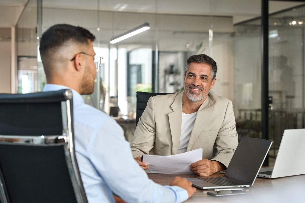 A person in a light shirt interviews with a smiling colleague holding papers in a bright, modern office.