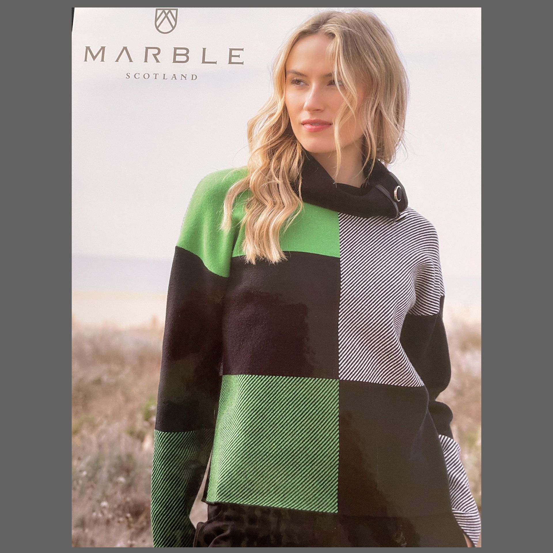 Woman wearing a color block sweater. Black, green, and striped sections, with the 