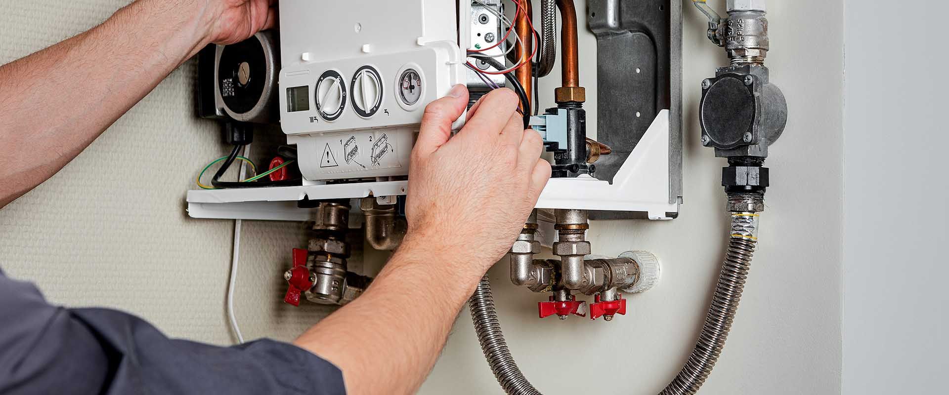 A man is fixing a boiler with a hose attached to it.