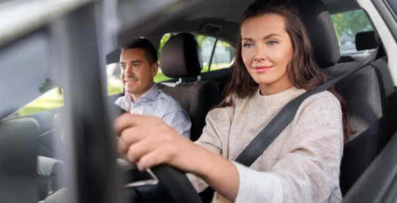 A person drives a car while another person sits in the passenger seat, both appearing calm and focused.