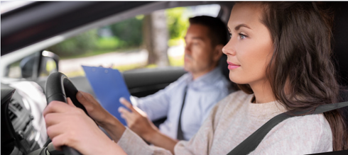 A driving instructor holds a clipboard while a student drives a car.