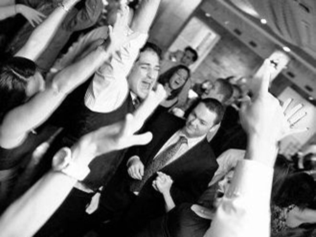 People dancing at a party, arms raised in the air, joyful expressions. Black and white.