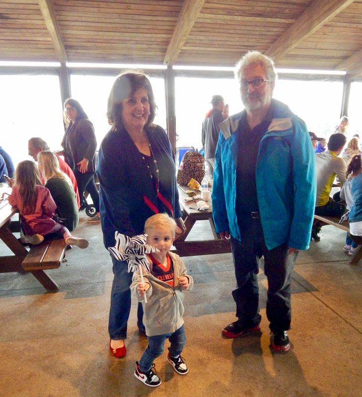 Woman, toddler, and man stand under a shelter. The woman wears jeans, a top, and red shoes. The man wears a blue jacket.