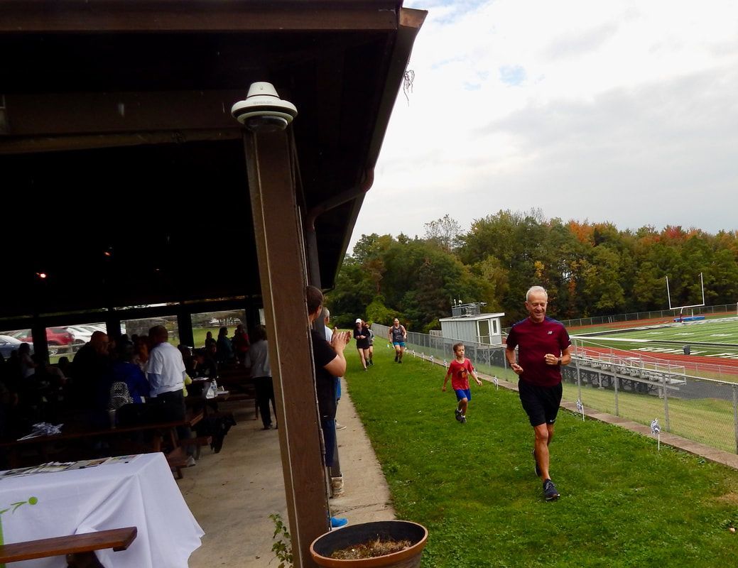People running on grass next to a pavilion and a track.