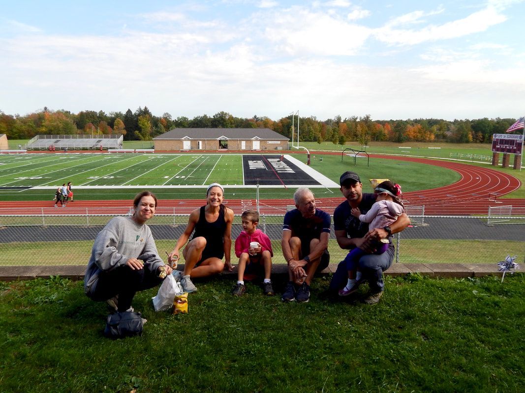 Group of people on grass with a football field in the background, autumn colors.
