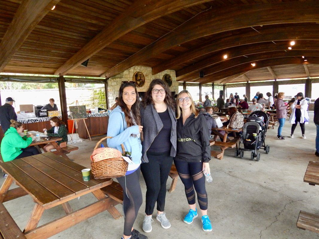 Three people pose in a covered picnic area with other people. One holds a basket.