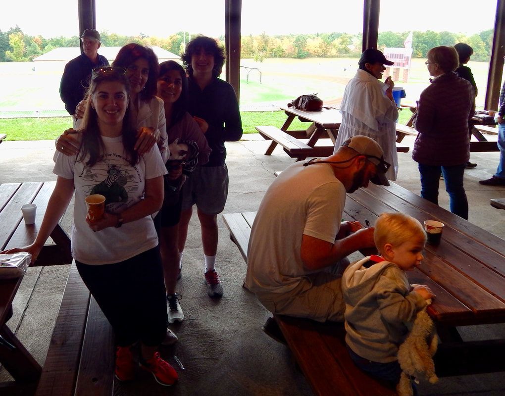 People gathered at picnic tables under a pavilion, drinking beverages.