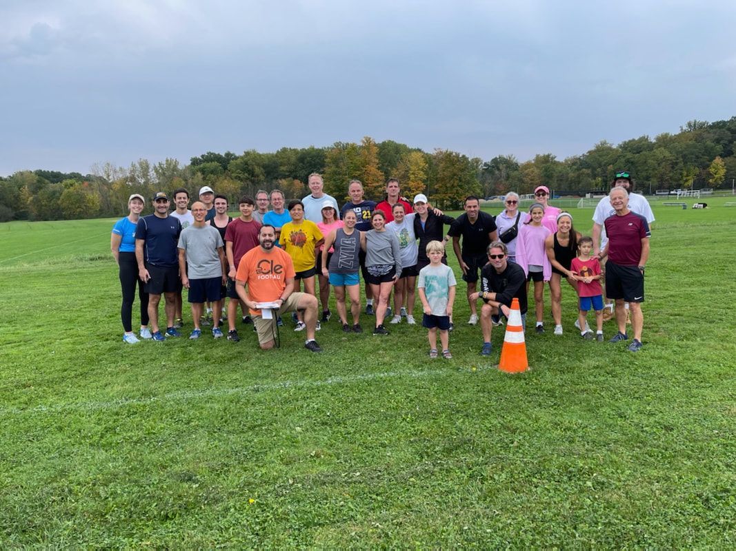 Group of people standing on a grassy field, posing for a photo near a white line and a traffic cone. Overcast sky.