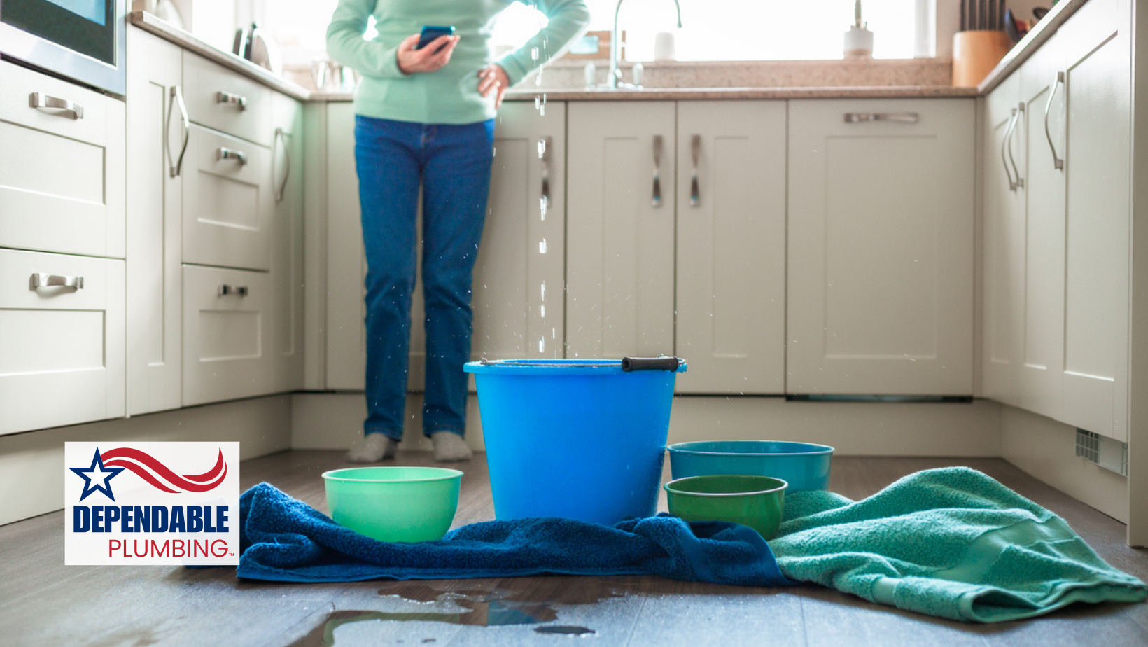 Kitchen with overflowing leak; person using phone. Buckets and towels on the floor.