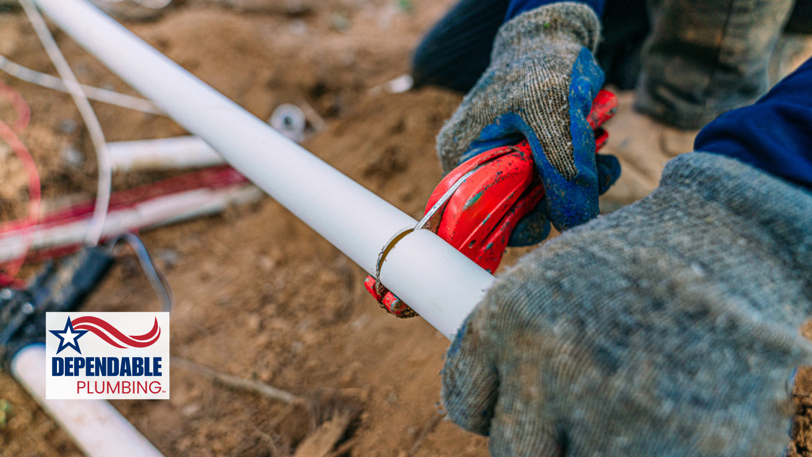 Person cutting white PVC pipe with a red pipe cutter outdoors.