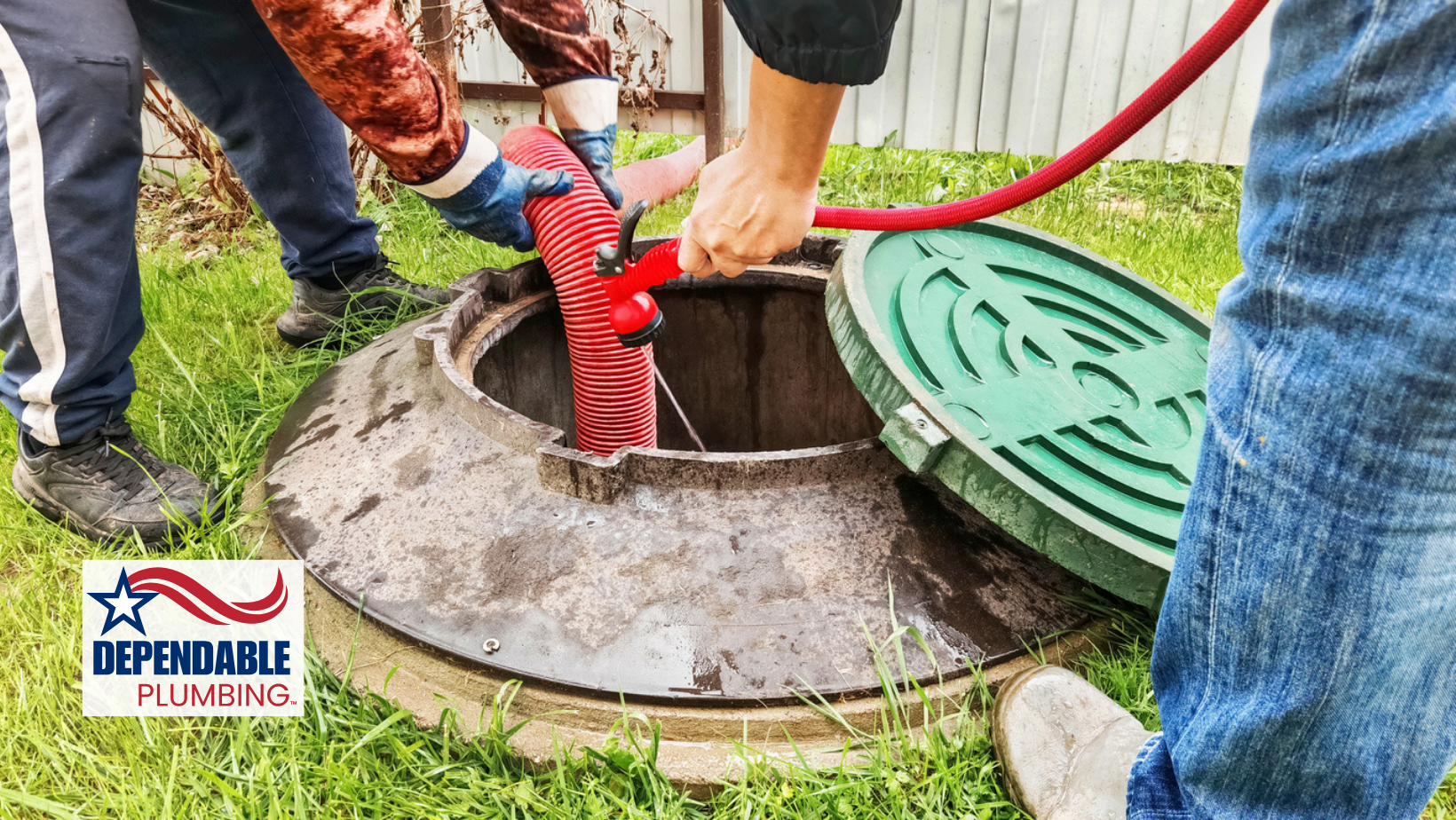 Two people using a red hose to clean a septic tank in a grassy yard.