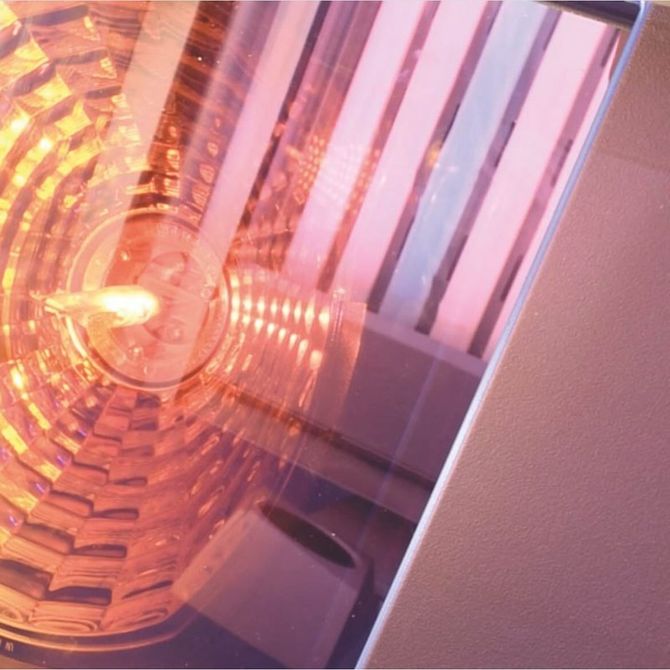 Primo piano di un semaforo circolare arancione brillante, con vetro riflettente e decorato, posizionato accanto a un pannello metallico.