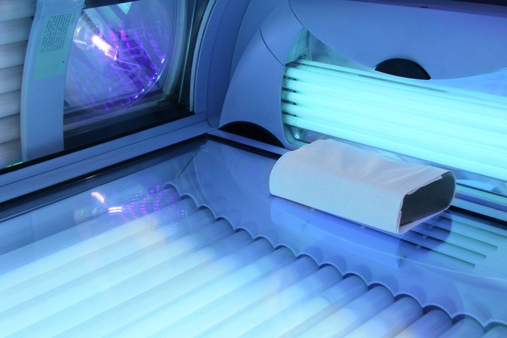 Un lettino abbronzante con lampade UV luminose e un cuscino bianco sulla superficie in acrilico.