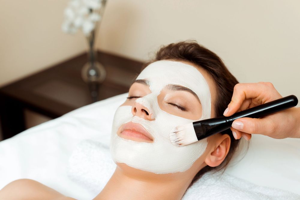In un centro benessere, una persona si fa applicare una maschera di argilla bianca sul viso con un pennello da un'altra persona.