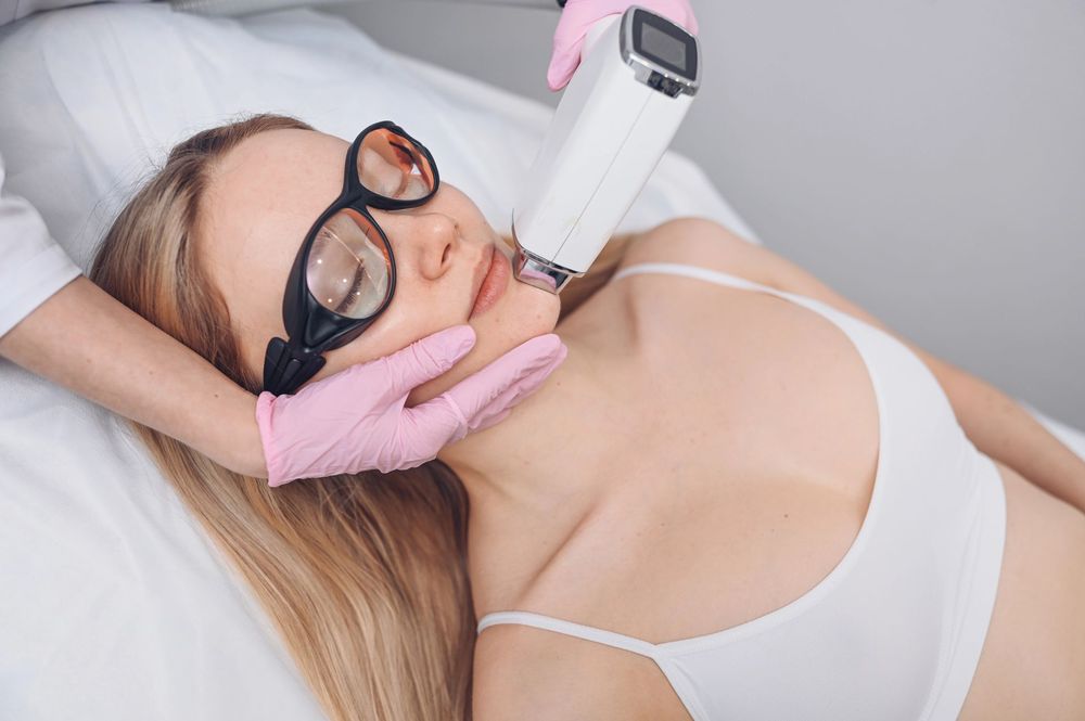 Una persona con occhiali protettivi riceve un trattamento laser sulla mascella da un tecnico con guanti rosa.