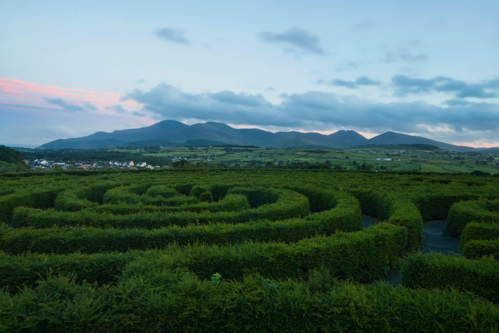 A green hedge maze with mountain backdrop at dusk.