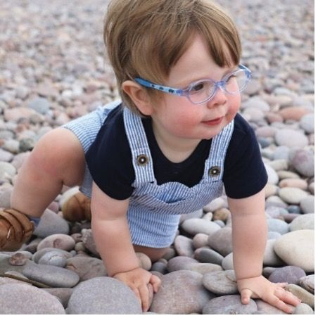 Toddler in glasses, overalls, crawling on rocks, looking to the side.