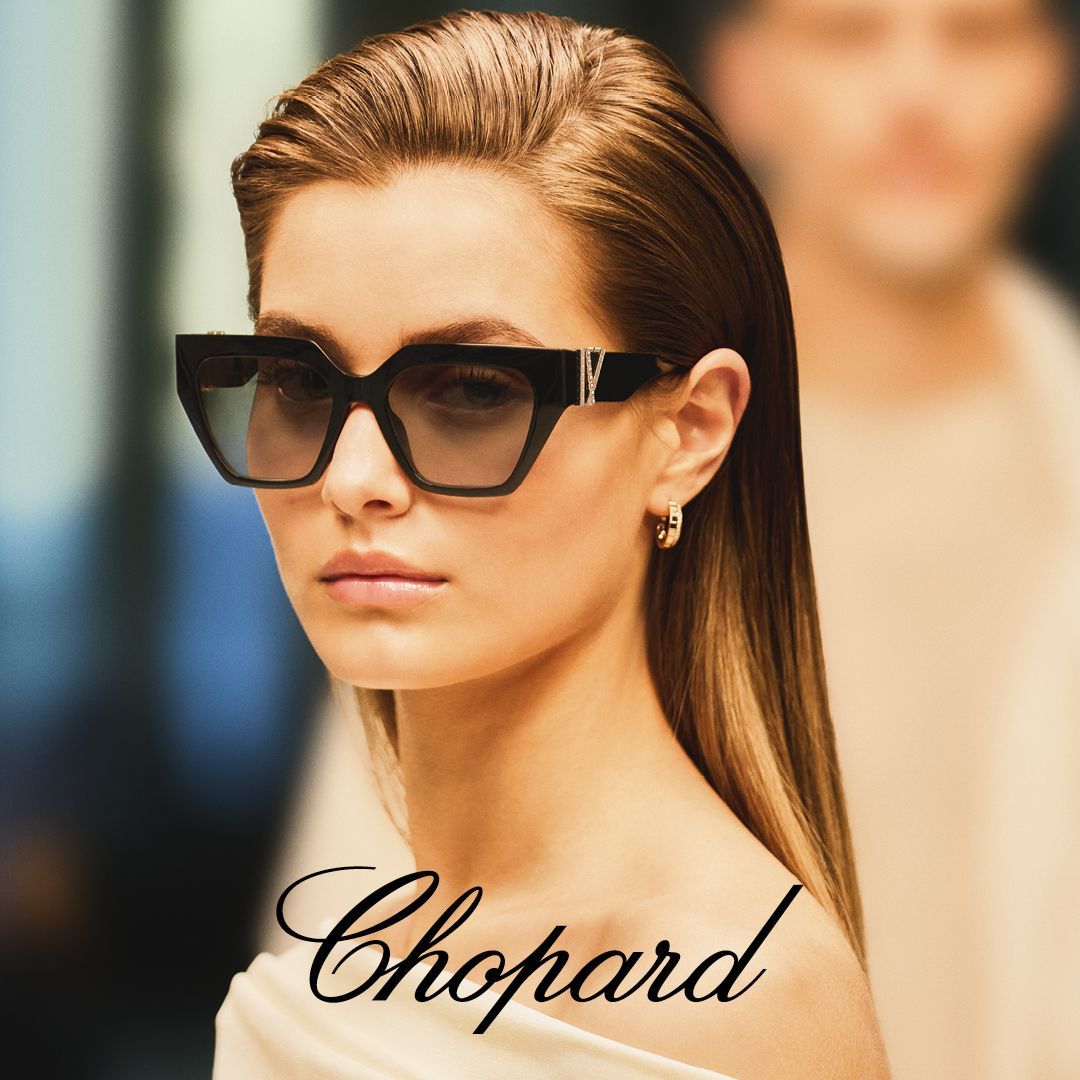 Woman wearing Chopard sunglasses, looking forward, with a blurred person in the background.
