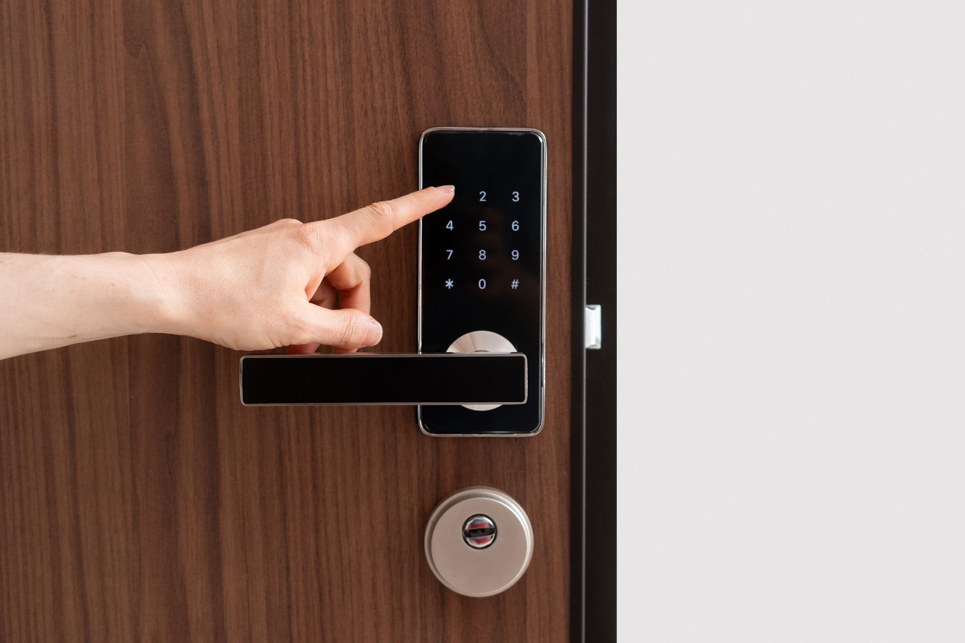 Hand entering code on a black keypad door lock on a brown door.