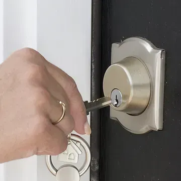 Hand inserting key into a silver door lock, attached to a black door, with a house-shaped keychain.