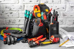 A tool bag filled with electrical tools and gloves on a table.