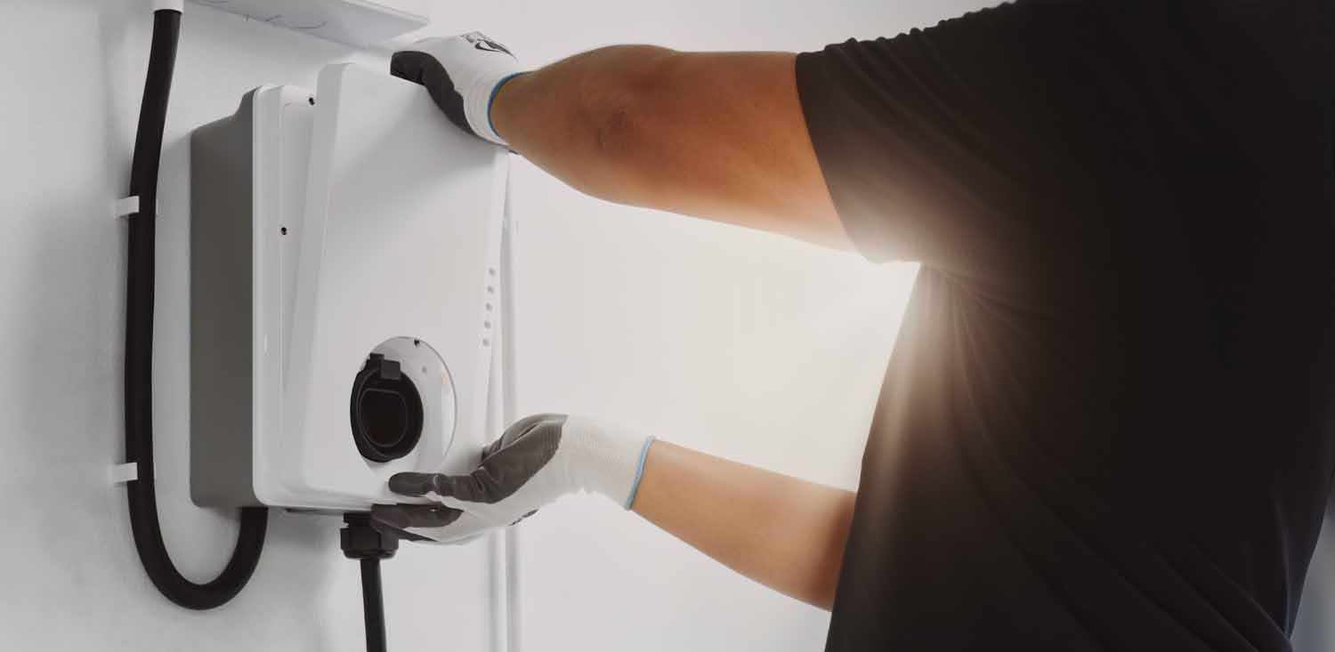 A man is installing an electric car charger on a wall.