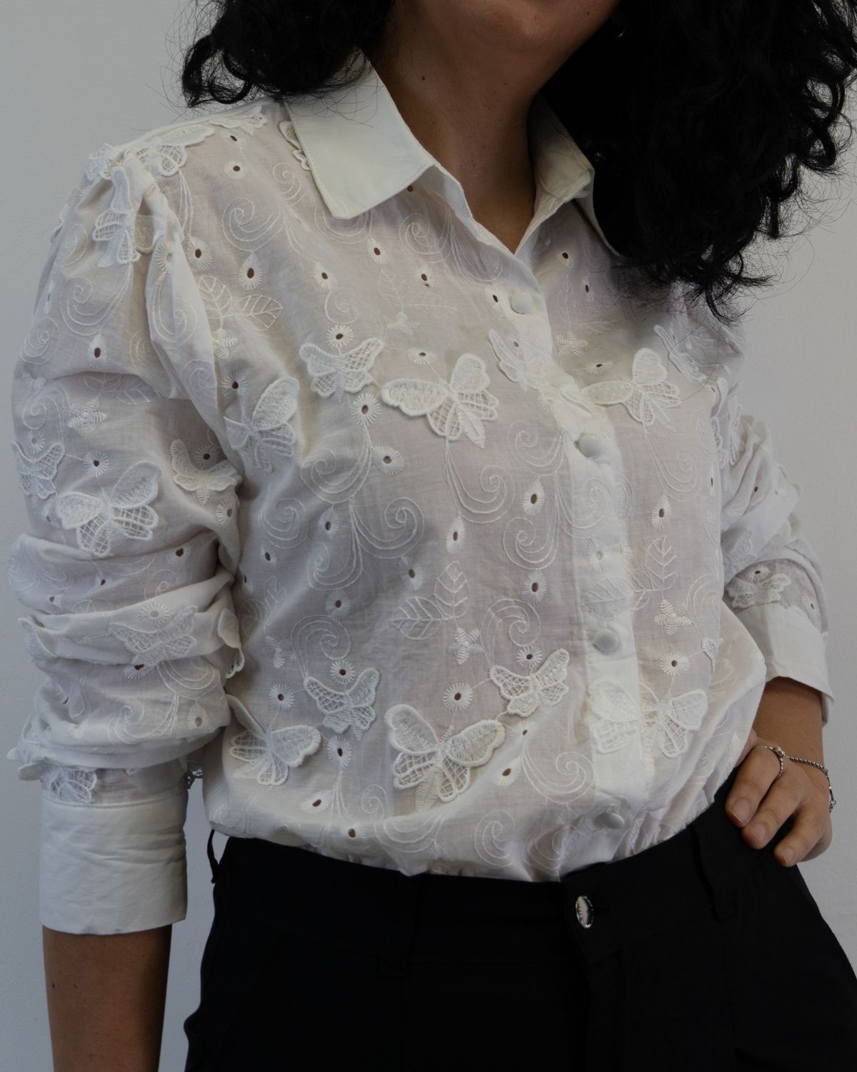 Mujer con blusa blanca bordada con mariposas, pantalón oscuro.