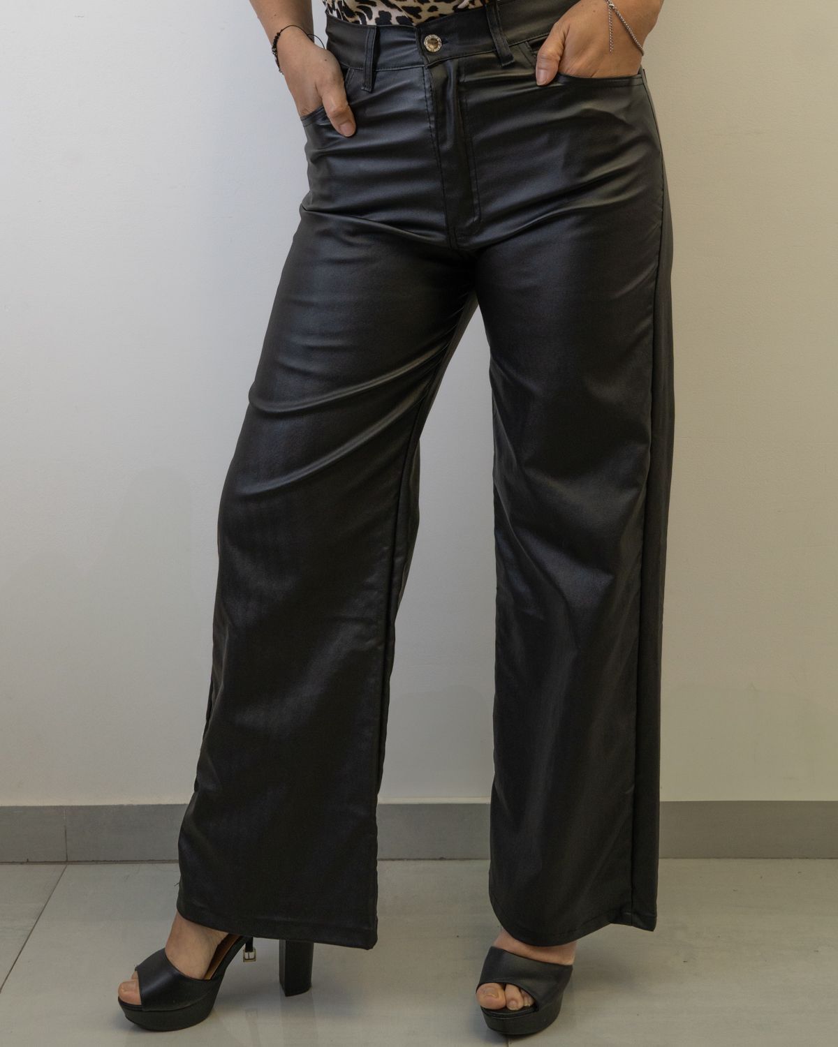 Mujer con pantalones de cuero negro y tacones de plataforma, manos en los bolsillos.