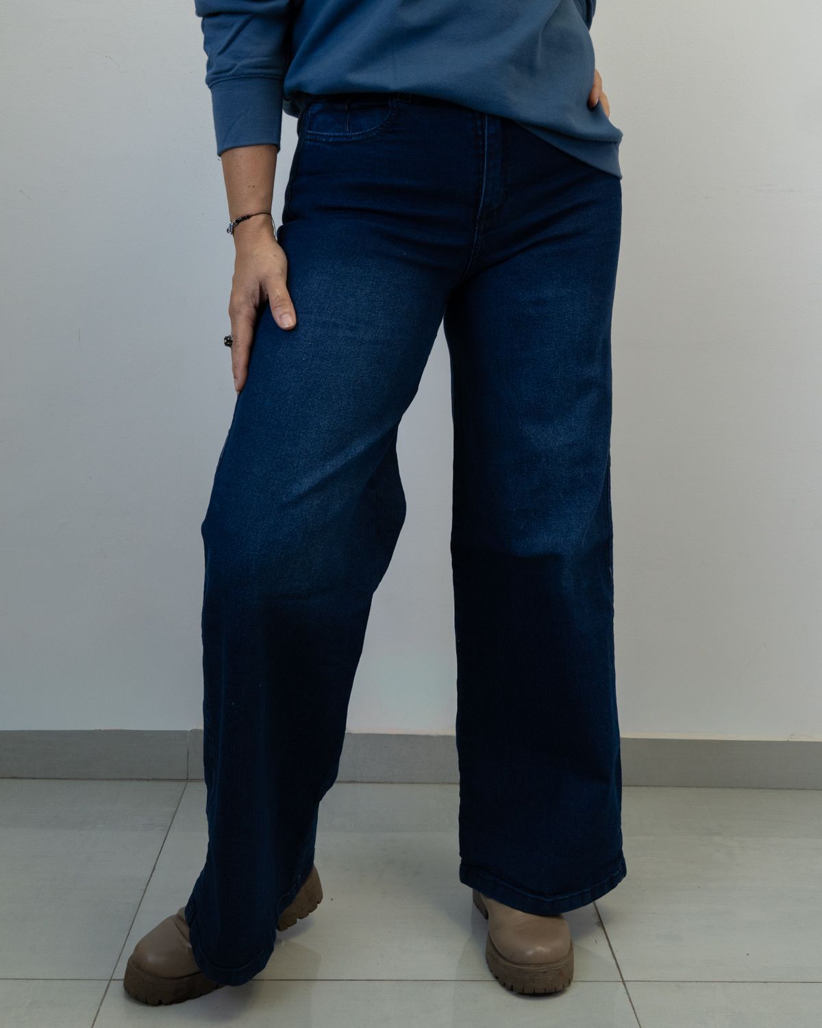 Persona que viste jeans azules y suéter, de pie con la mano en el bolsillo.