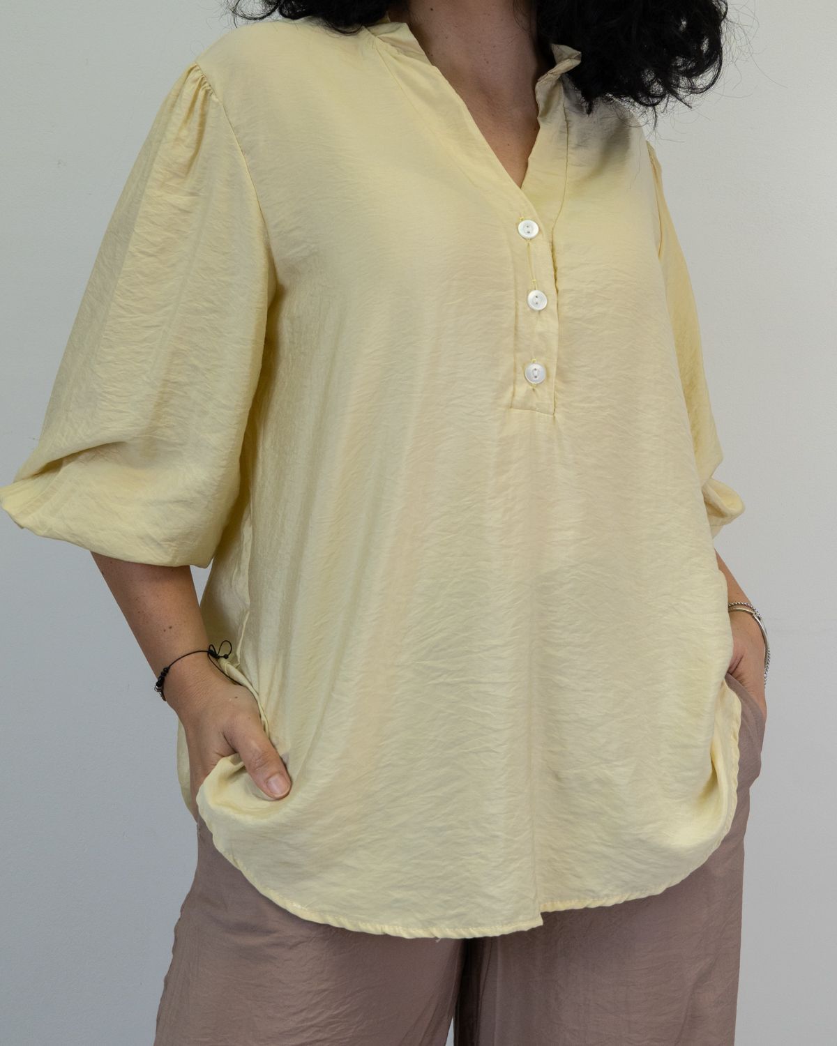 Mujer con blusa amarilla pálida y cuello mandarín y manos en los bolsillos.